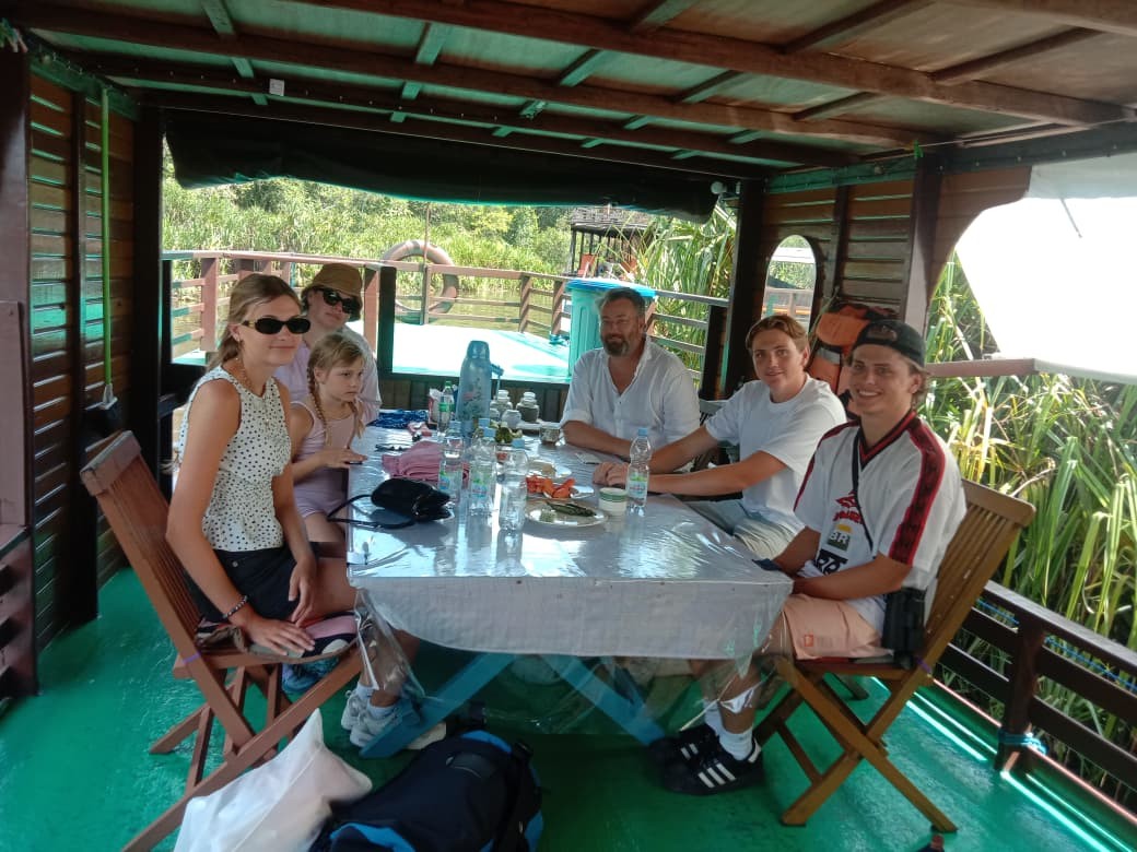 Guests gathered for a meal on the klotok lower deck with jungle riverbank views.