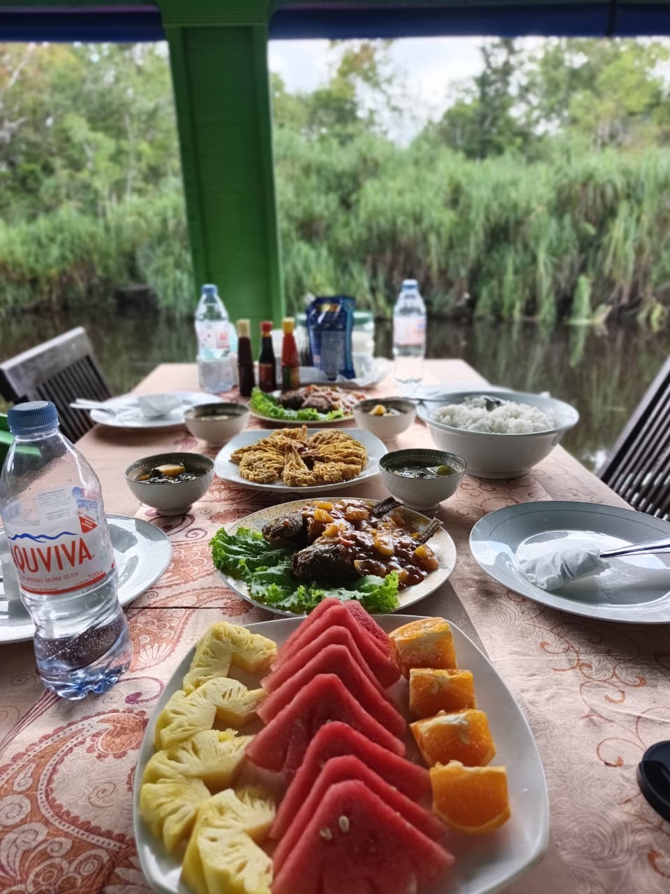Freshly cut watermelon, pineapple, and papaya alongside a full klotok lunch spread by the river.